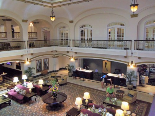 A spacious hotel lobby with elegant decor, seating areas, and a reception desk, featuring large windows and plants.