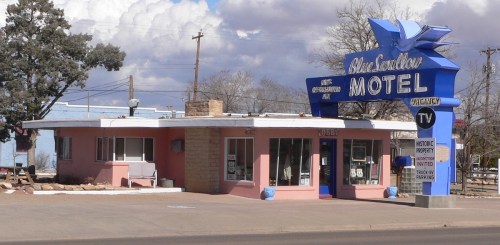 A retro-style motel with a blue and pink exterior, featuring a large sign that reads "Blue Swallow Motel."