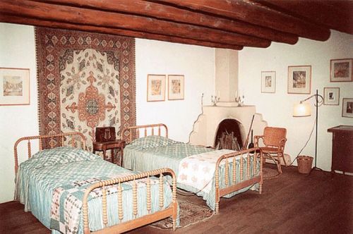 A cozy bedroom with two twin beds, a decorative wall hanging, a fireplace, and warm wooden beams overhead.