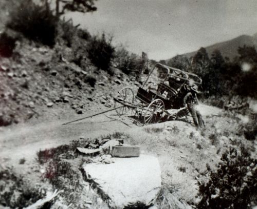 A vintage black-and-white photo of an old cart on a dirt path surrounded by rocky terrain and sparse vegetation.
