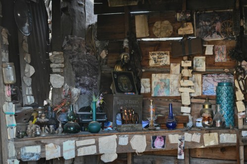 A rustic wooden shelf filled with various artifacts, candles, and notes, set against a textured wall.