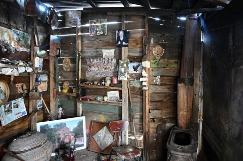 A rustic interior with wooden walls, various artifacts, and a chair, creating a nostalgic and cluttered atmosphere.