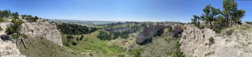 Panoramic view of a lush green valley surrounded by rocky cliffs under a clear blue sky.