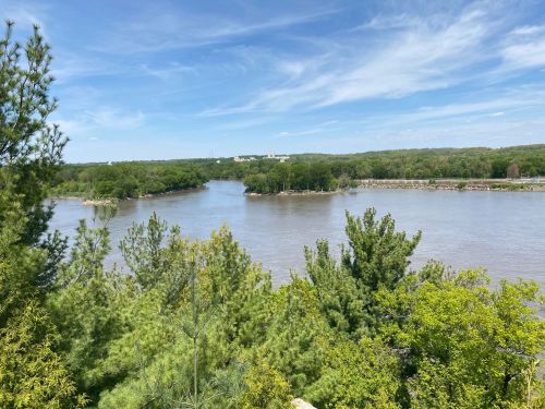 A scenic view of a river winding through lush greenery under a blue sky with scattered clouds.