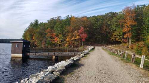 A scenic lakeside path with colorful autumn trees and a small wooden structure by the water.