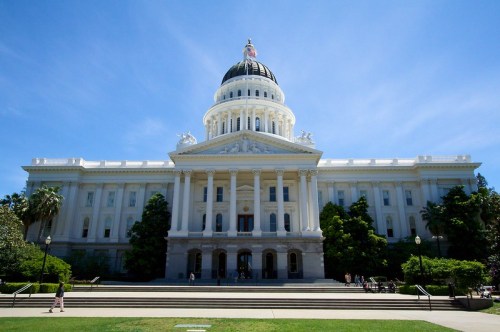 The California State Capitol building, featuring a large dome and classical architecture, set against a clear blue sky.