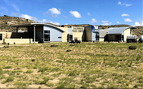 A modern building with a sign reading "California Trail Center," surrounded by open grassland and blue skies.