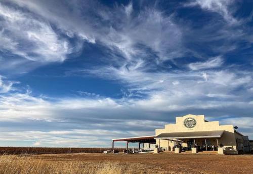 A rustic building with a large porch sits under a dramatic sky filled with clouds, surrounded by open land.