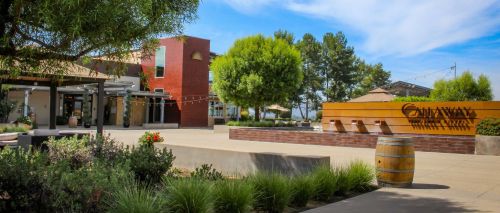 Exterior view of a winery with modern architecture, landscaped gardens, and a wooden sign displaying the winery's name.