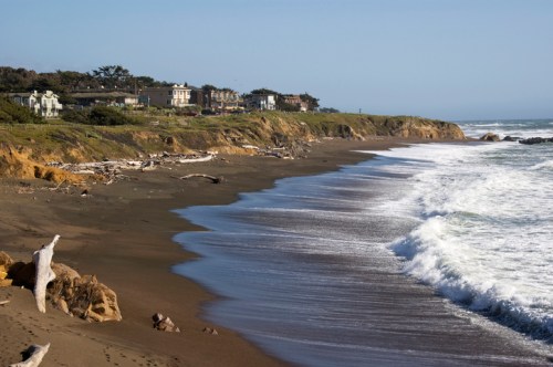 A sandy beach with gentle waves, cliffs in the background, and a clear blue sky.