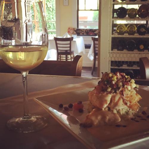 A glass of white wine beside a plated dish topped with colorful garnishes, set in a cozy dining environment.