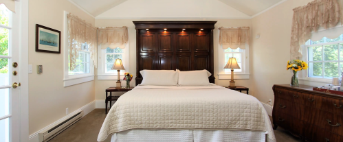 Cozy bedroom with a large bed, wooden headboard, two lamps, and natural light from windows. Decorated with soft colors.