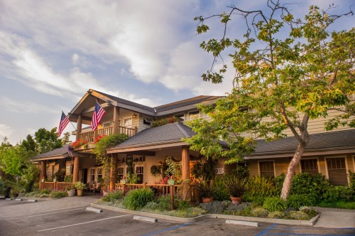 A charming building with American flags, surrounded by greenery and potted plants, under a partly cloudy sky.
