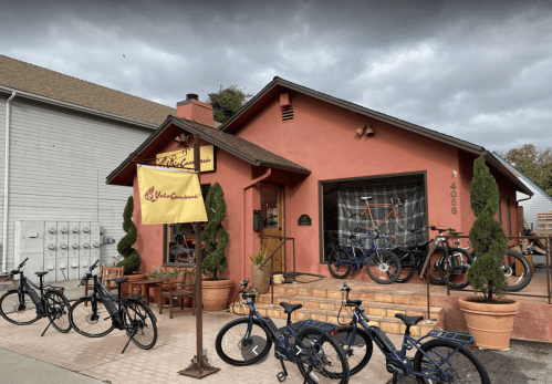A quaint pink building with bicycles outside, featuring a sign and potted plants, under a cloudy sky.