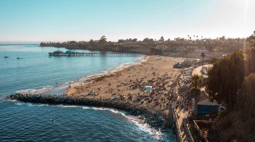 Aerial view of a beach with a pier, people enjoying the sun, and calm waters under a clear blue sky.