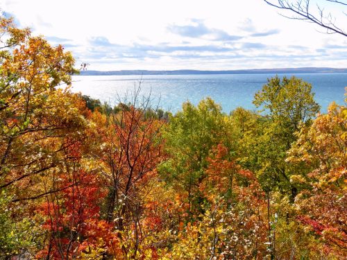 Vibrant autumn foliage in shades of red, orange, and yellow overlooking a calm lake under a cloudy sky.