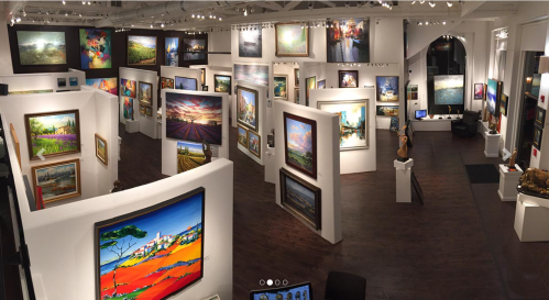 A panoramic view of an art gallery featuring colorful paintings displayed on white walls.