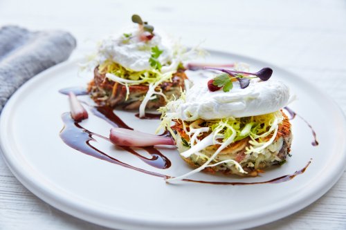 Two crispy vegetable patties topped with poached eggs, shredded greens, and drizzled with a balsamic reduction on a plate.