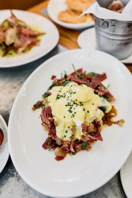 A plate of corned beef hash topped with poached eggs and hollandaise sauce, garnished with chives.