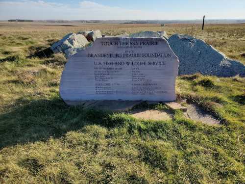 A stone monument in a grassy field, detailing the Touch the Sky Prairie project and its sponsors.