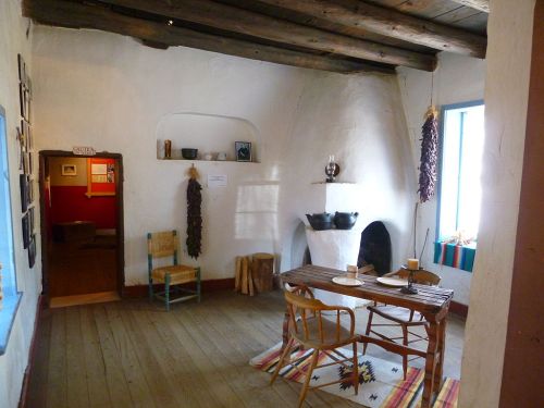 Cozy interior of a rustic room with a wooden table, chairs, and a fireplace, decorated with traditional items.