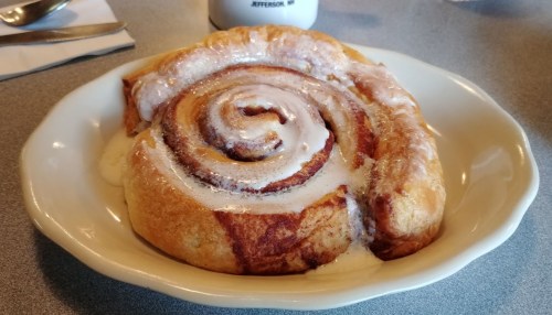 A freshly baked cinnamon roll with creamy icing, served on a white plate.