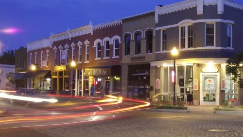 A charming street scene at dusk, featuring colorful storefronts and light trails from passing cars.