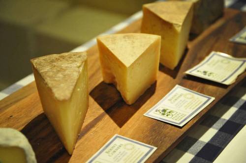 A wooden platter displaying various cheese wedges with labels, set on a checkered tablecloth.