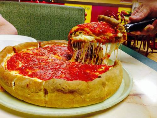 A slice of cheesy deep-dish pizza being lifted from a whole pizza, topped with marinara sauce.