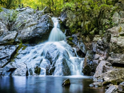A serene waterfall cascading over rocks into a calm pool, surrounded by lush greenery and trees.