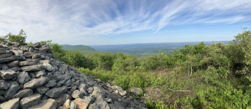 A panoramic view of rolling hills and valleys under a blue sky, with a stone pile in the foreground.