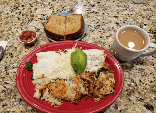 A plate with an omelette, hash browns, a slice of toast, salsa, and a cup of coffee on a granite table.