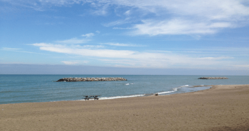 A serene beach scene with gentle waves, a sandy shore, and distant rocky formations under a blue sky.