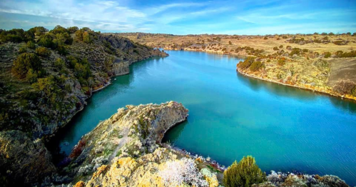 A serene river winding through rocky terrain and lush greenery under a clear blue sky.
