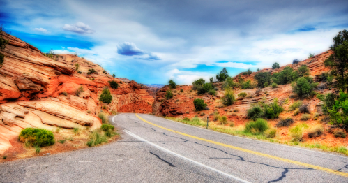 A winding road through colorful rock formations and greenery under a cloudy sky.