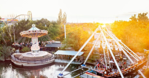 A vibrant amusement park scene at sunset, featuring a carousel and a swinging ship ride surrounded by trees.