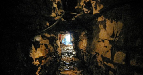 A dimly lit underground tunnel with rough stone walls, leading to a distant light source.