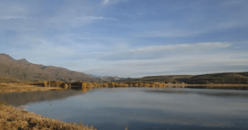 A serene lake surrounded by mountains and autumn trees under a clear blue sky.