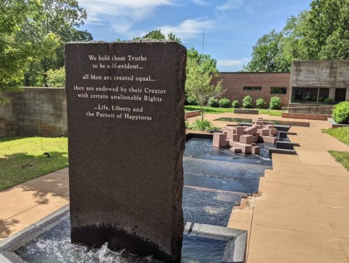 A stone monument with an inscription about equality and rights, surrounded by a water feature and greenery.