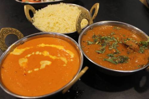 Two bowls of curry with a swirl of cream, garnished with herbs, alongside a bowl of fluffy white rice.