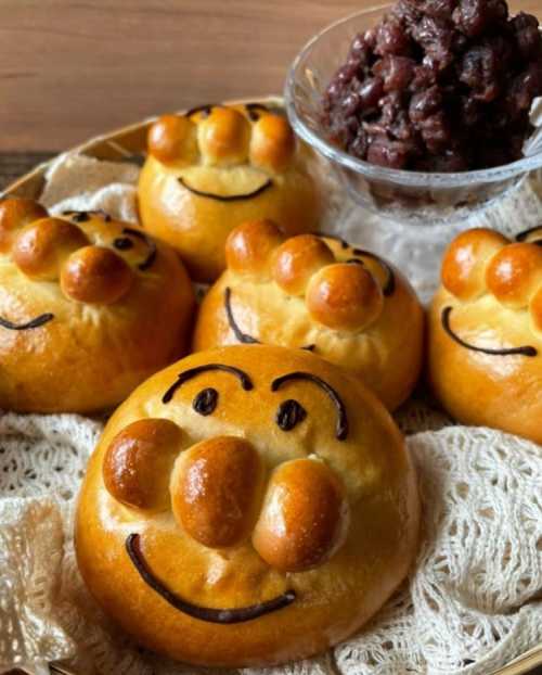 A plate of smiling, round buns with cartoonish faces, accompanied by a bowl of red bean paste.