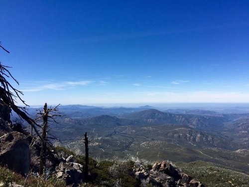 A panoramic view of mountains and valleys under a clear blue sky, with rocky terrain in the foreground.