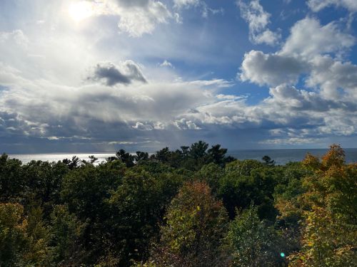 A scenic view of a lake surrounded by trees under a partly cloudy sky with sunlight breaking through.