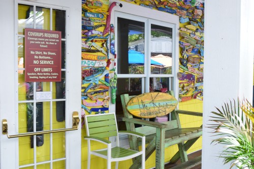 A colorful outdoor seating area with a surfboard and a sign about dress code and service rules.