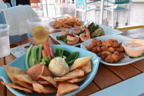 A colorful spread of appetizers including shrimp, fried calamari, vegetables, and chips on a wooden table.