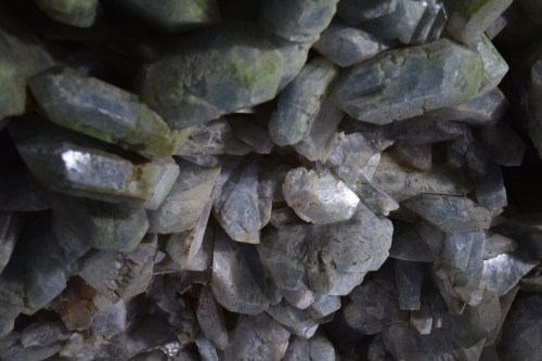 Close-up of shimmering, translucent crystals with various shades of gray and green, forming a natural mineral formation.