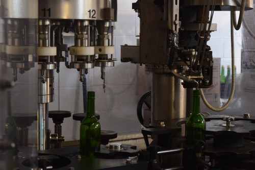 A close-up of a bottling machine with green bottles on a conveyor, showcasing industrial equipment in a factory setting.