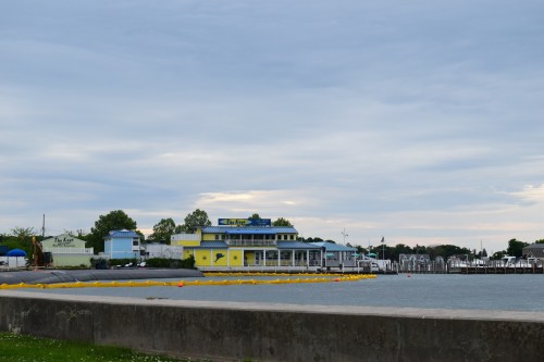 A waterfront view featuring a colorful building, cloudy sky, and boats docked in the background.