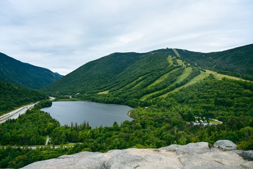 A scenic view of a lake surrounded by lush green mountains under a cloudy sky.