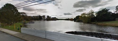 A calm river scene with trees along the banks, a cloudy sky, and a small boat on the water.